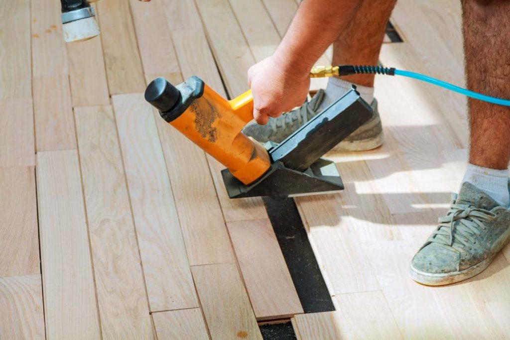 carpenter worker installing wood parquet board during flooring work with hammer